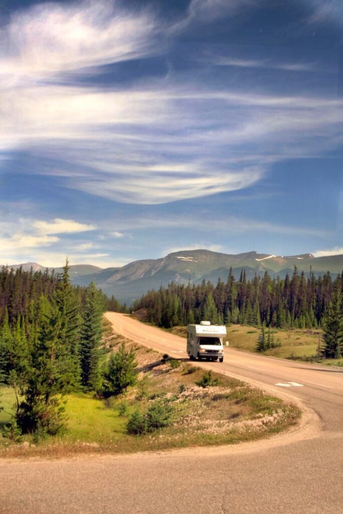 White camper van travels through stunning mountainous landscape under a blue sky.
