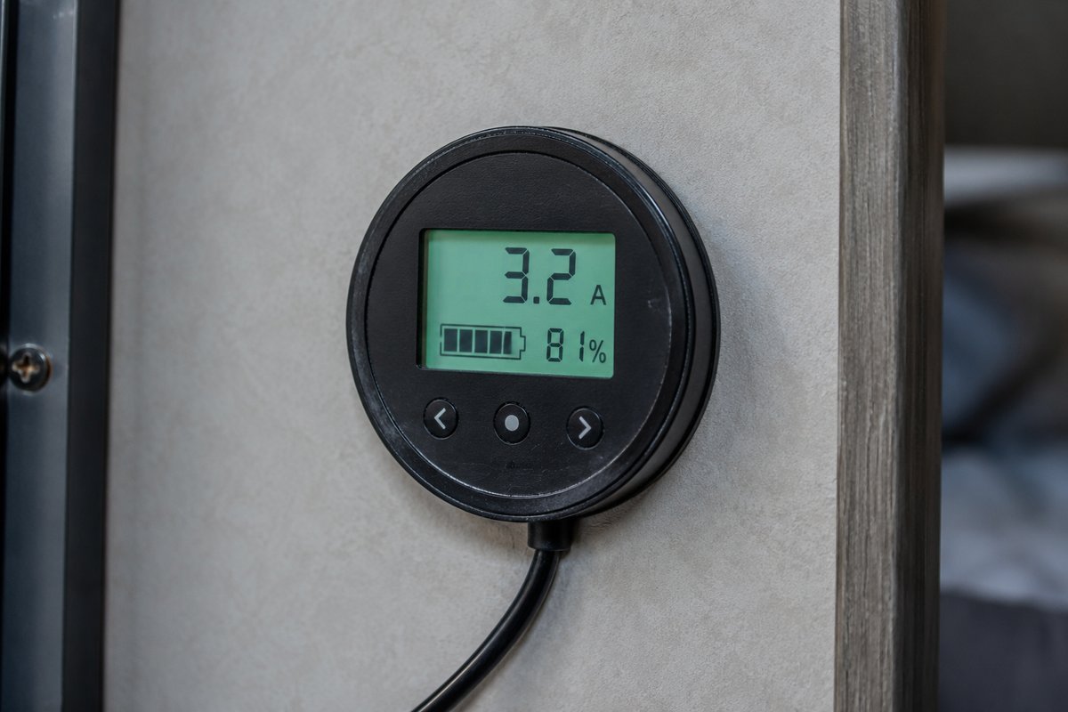A wall-mounted 12-volt battery monitor in a travel trailer reading 3.2 amps of draw with the battery at 81 percent, while a portable fridge runs.