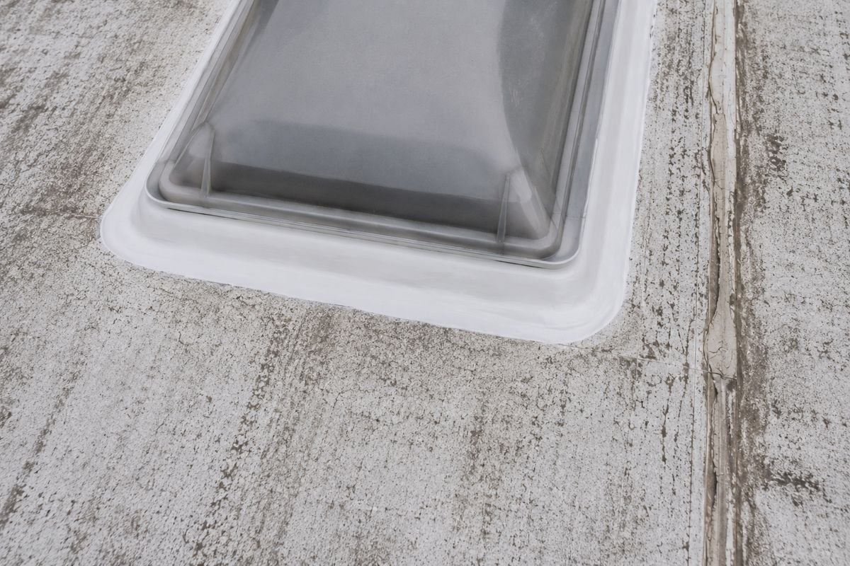 A fresh white bead of self leveling lap sealant flowed out smoothly around the flange of an RV roof vent, beside an older cracked bead on the seam