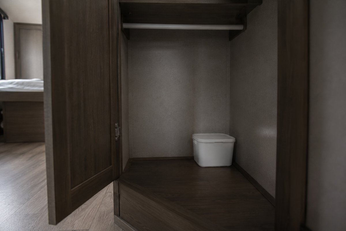 Moisture absorber tub used as an RV dehumidifier, standing in the back corner of a wardrobe against the outside wall, with the door propped open and the hanging rail empty.