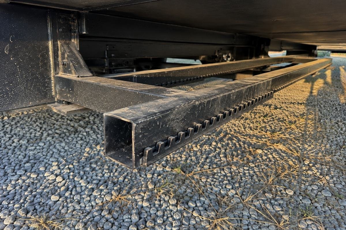 Two steel arm tubes with toothed gear racks running under the extended slide out room of a travel trailer