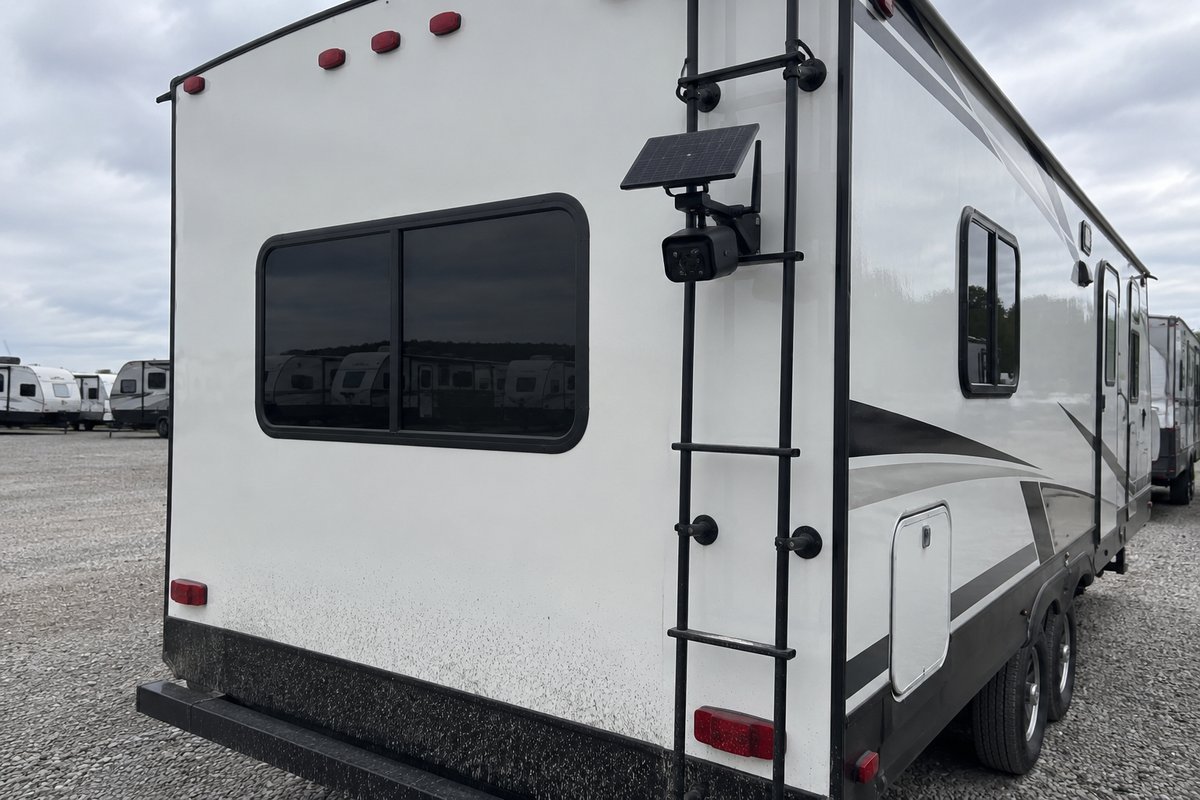 Solar-powered security camera clamped to the ladder rail on the back of a travel trailer in a storage lot