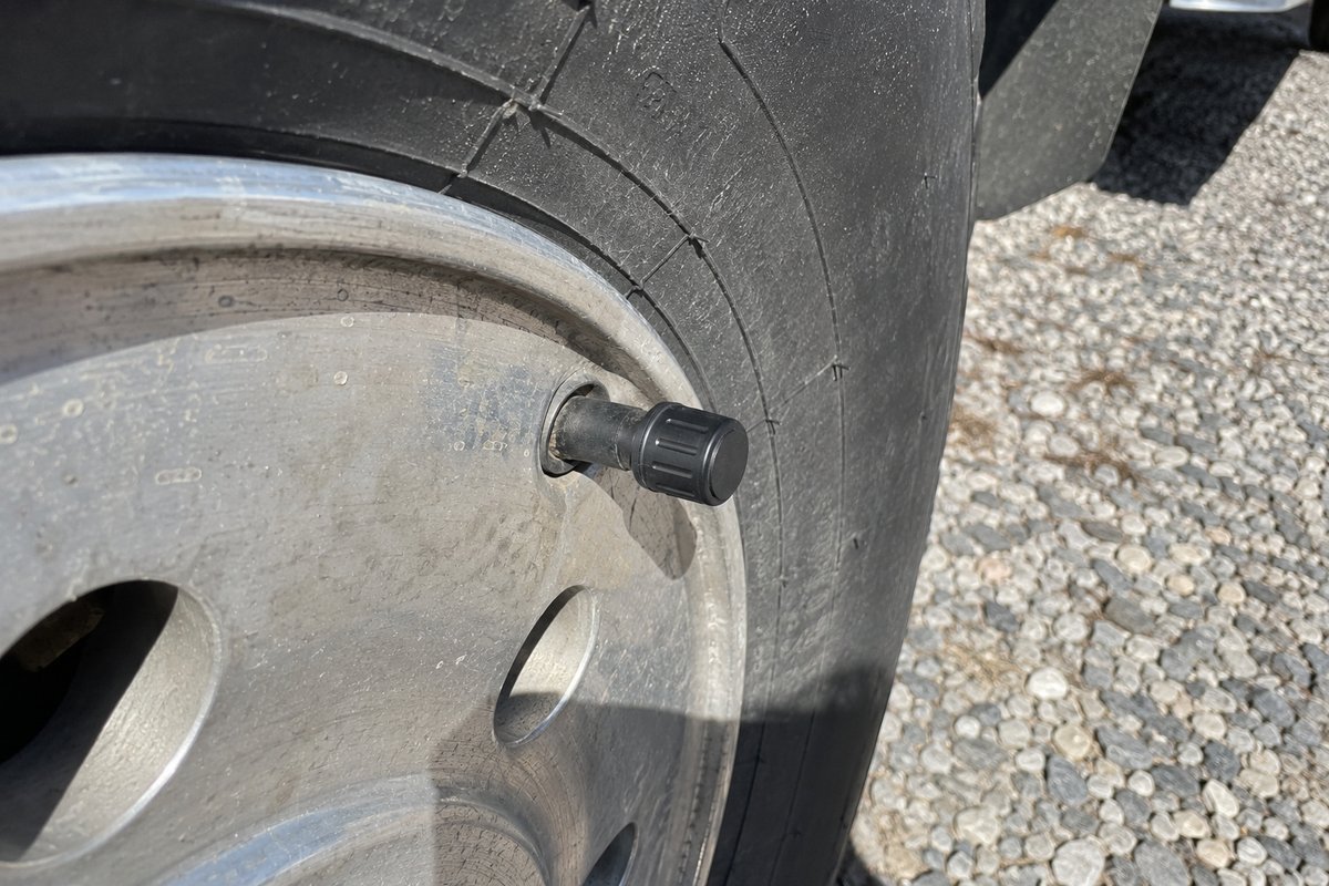 A TPMS for travel trailer wheels, its small black sensor screwed onto the valve stem of a dusty aluminum wheel in bright sun